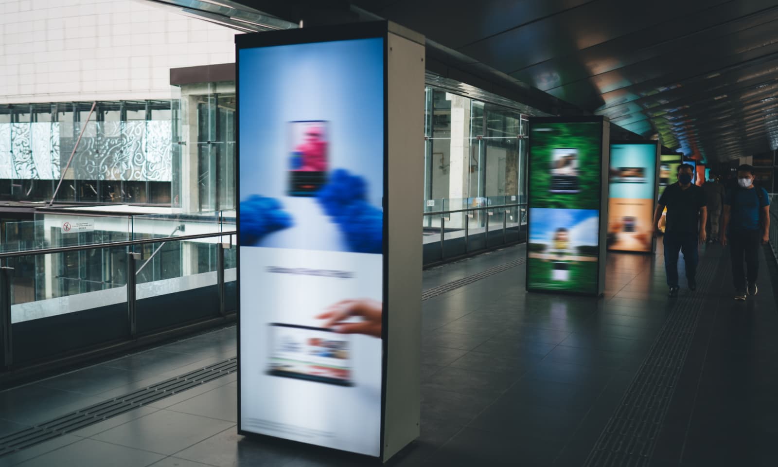 Group of people walking in public bridged walkway in station with blurred colorful digital signage