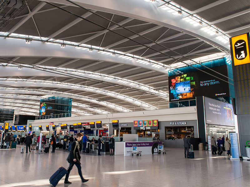 Heathrow Terminal 5 with passengers walking past giant LED screens