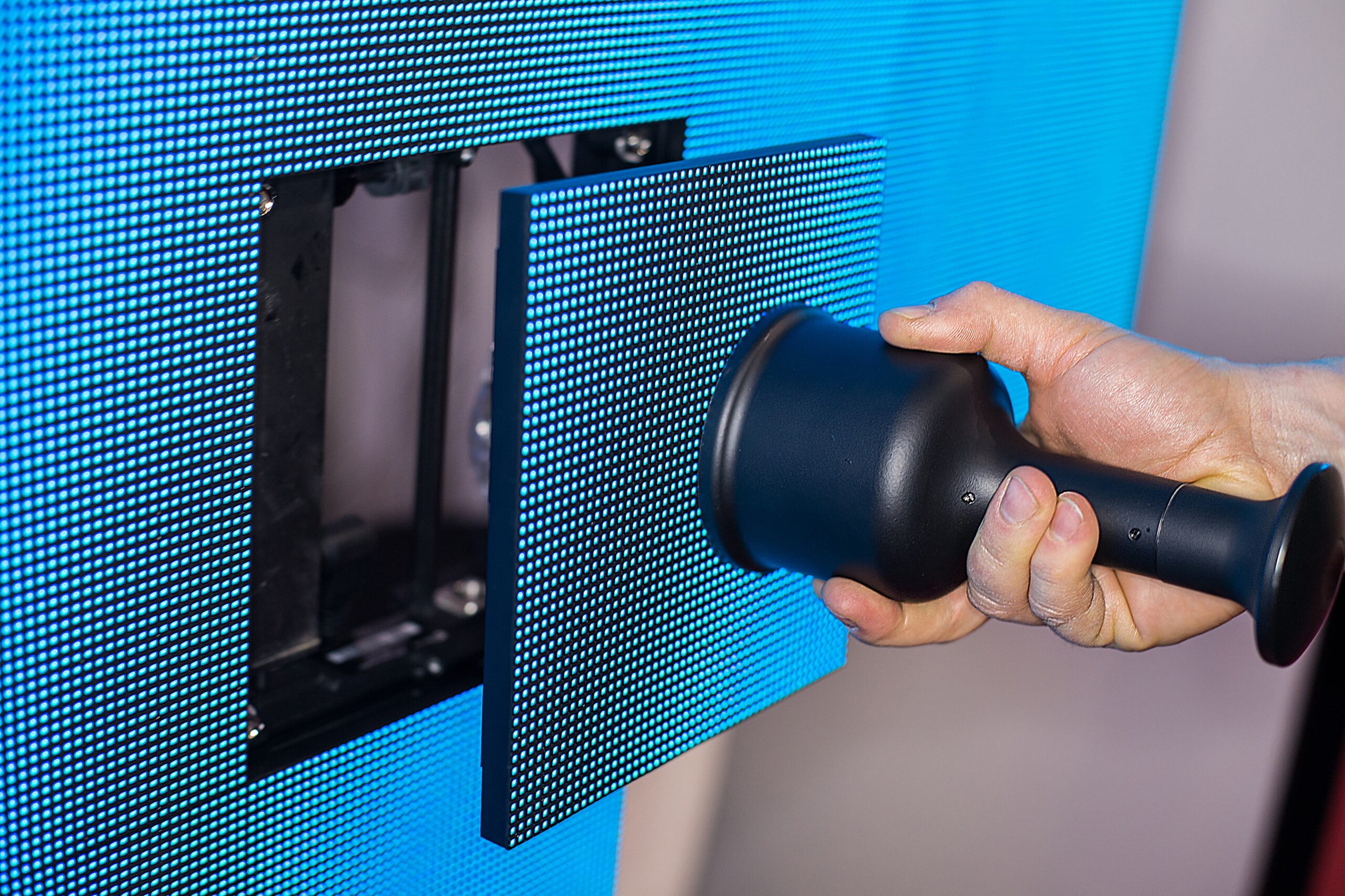 Technician using a suction tool to remove or install an LED display panel module on a digital signage screen